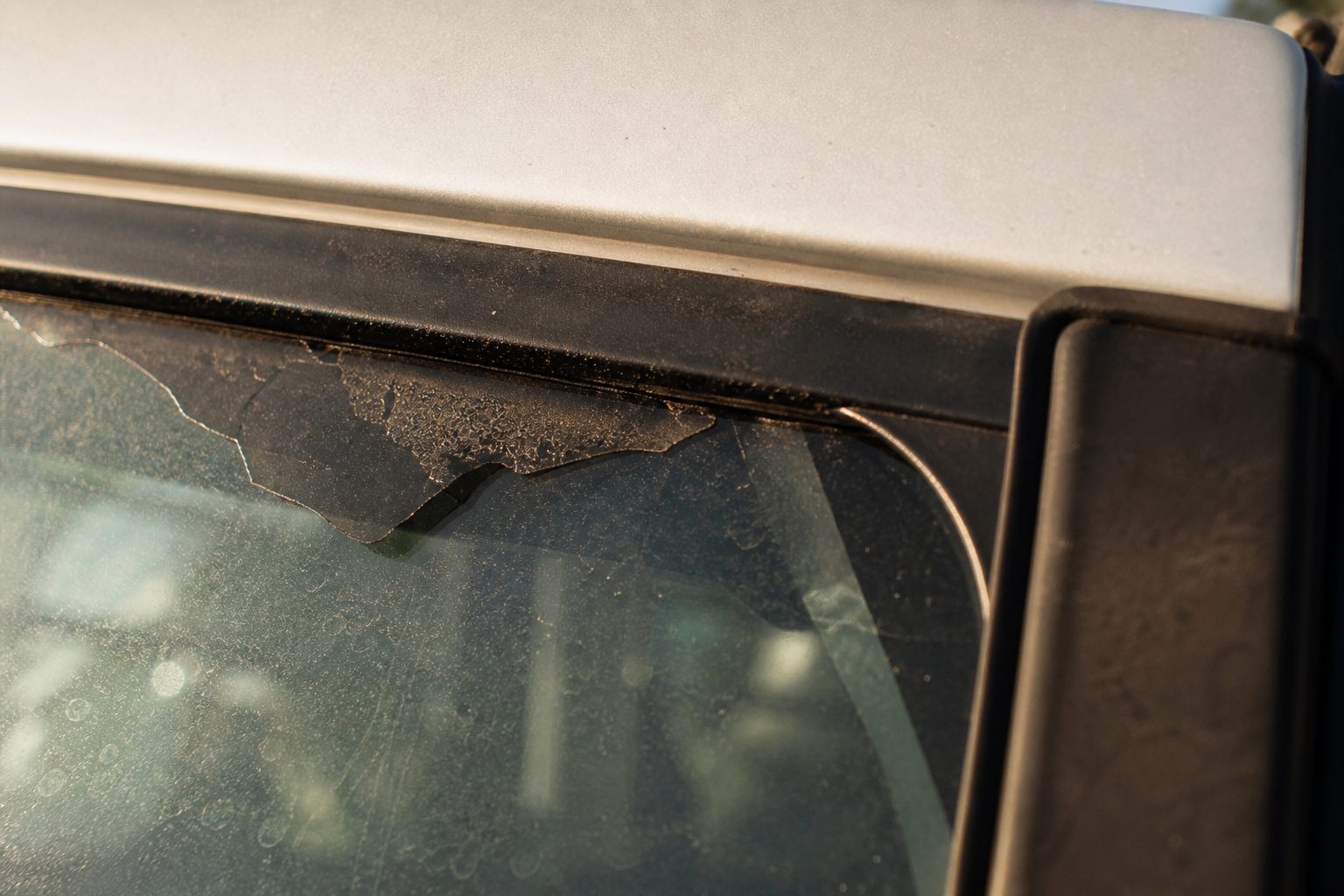 Close-up of an old car window tint edge lifting and peeling away from the glass