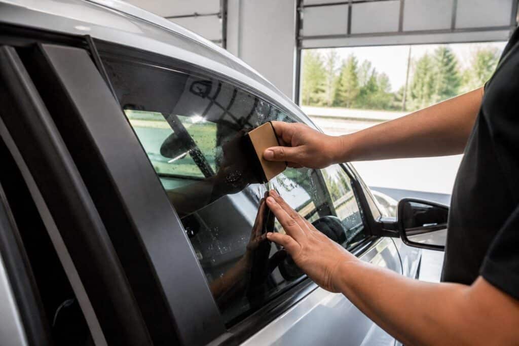 Professional installer applying dark window tint film to a car door window in a Punta Gorda auto shop