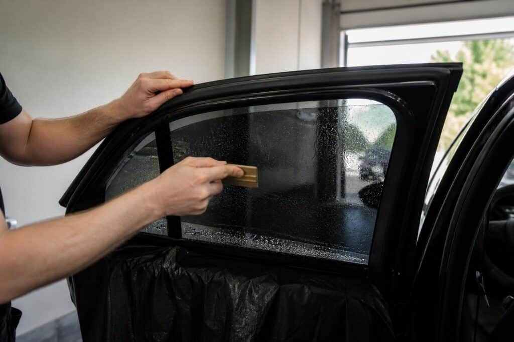 Installer squeegeeing water from freshly applied window tint film on a car window