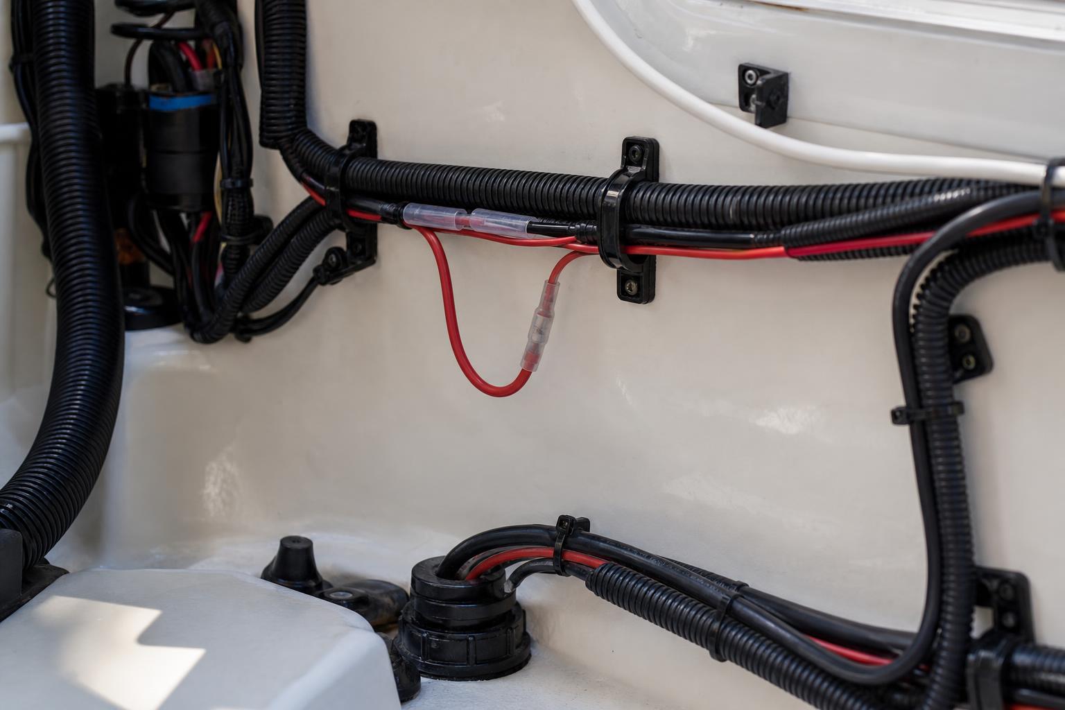 Marine wiring in split loom clipped along a boat console wall with a low loop in one lead